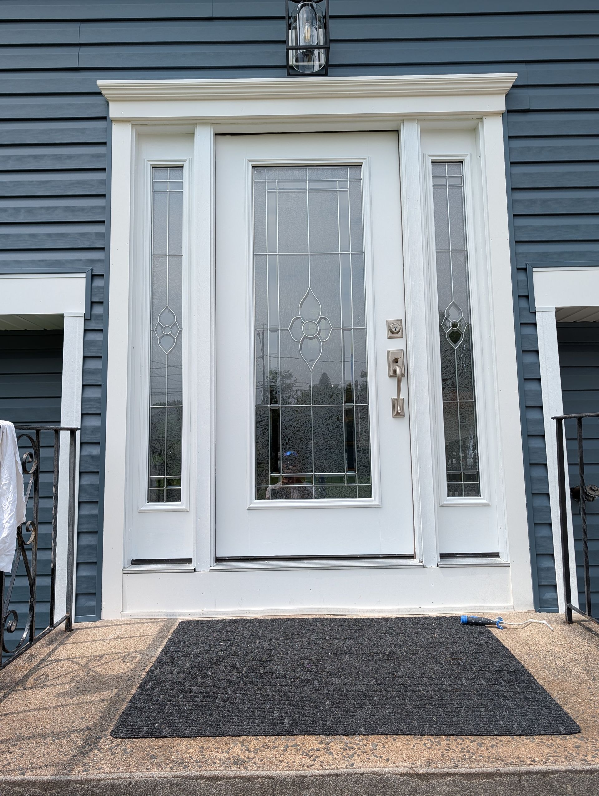 White front door with sidelights on blue house exterior and dark welcome mat on the porch