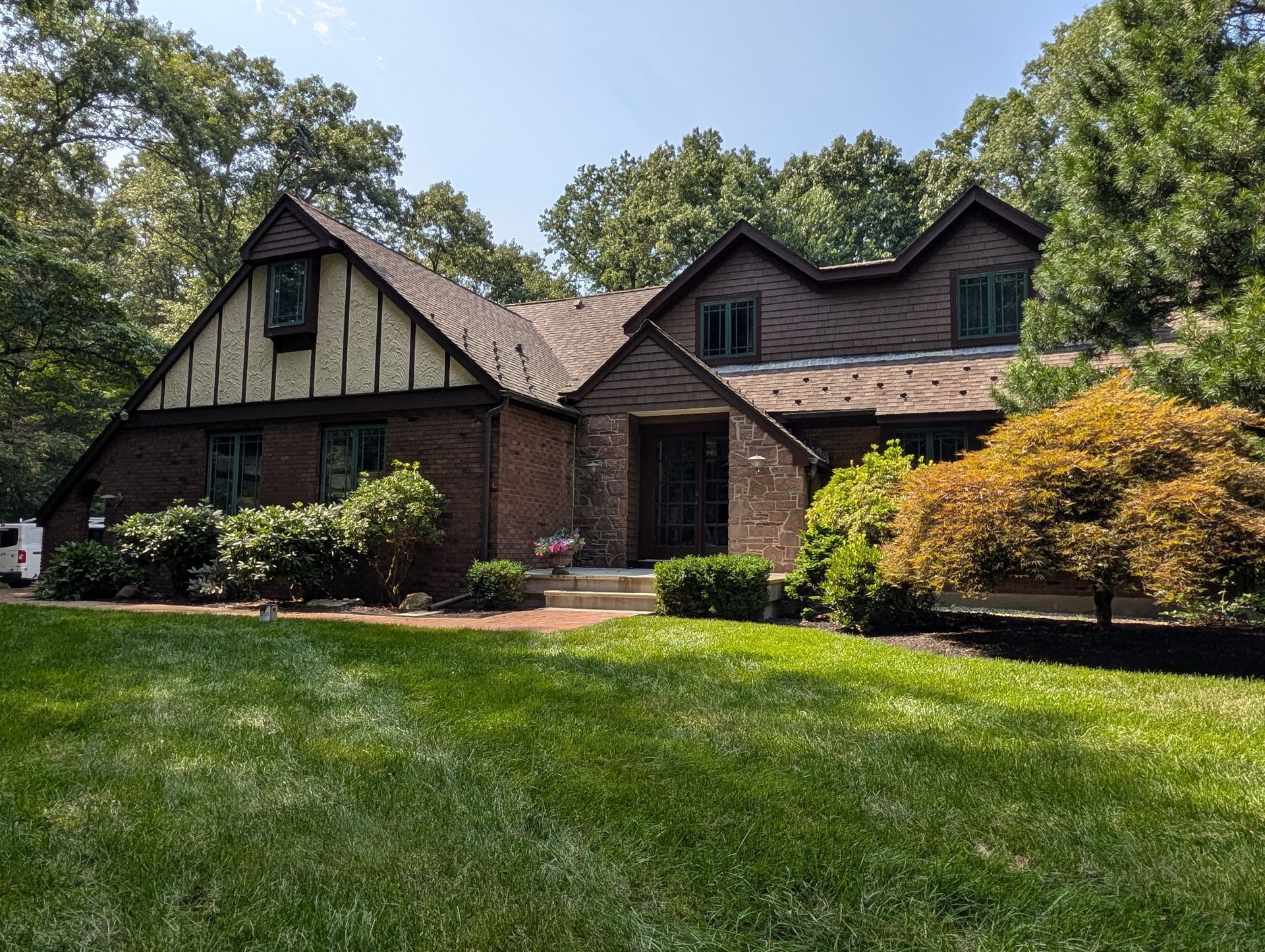 Brick and wood house with a green lawn and trees in front under a blue sky