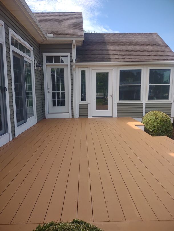 Wooden deck patio beside a house with white doors and windows, under a bright sky.