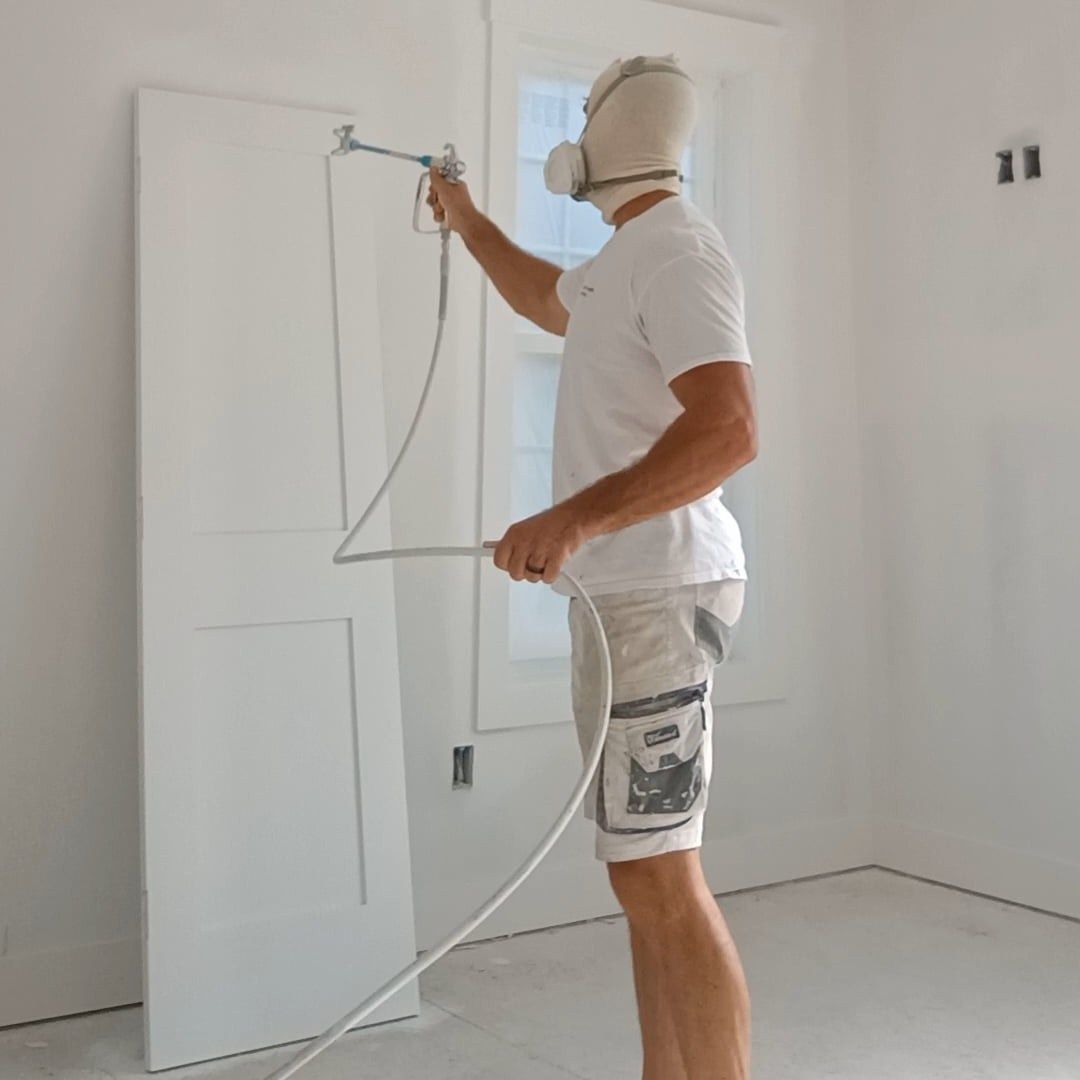 Painter spraying white door in a bright, unfinished room
