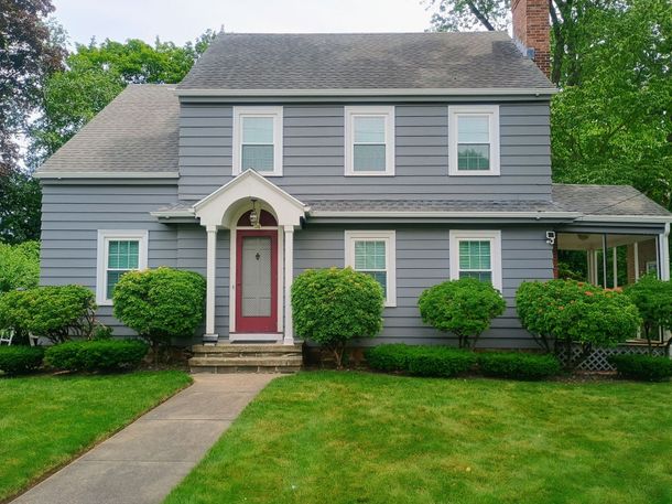 Gray two-story house with red front door, white trim, and a front lawn with bushes and walkway