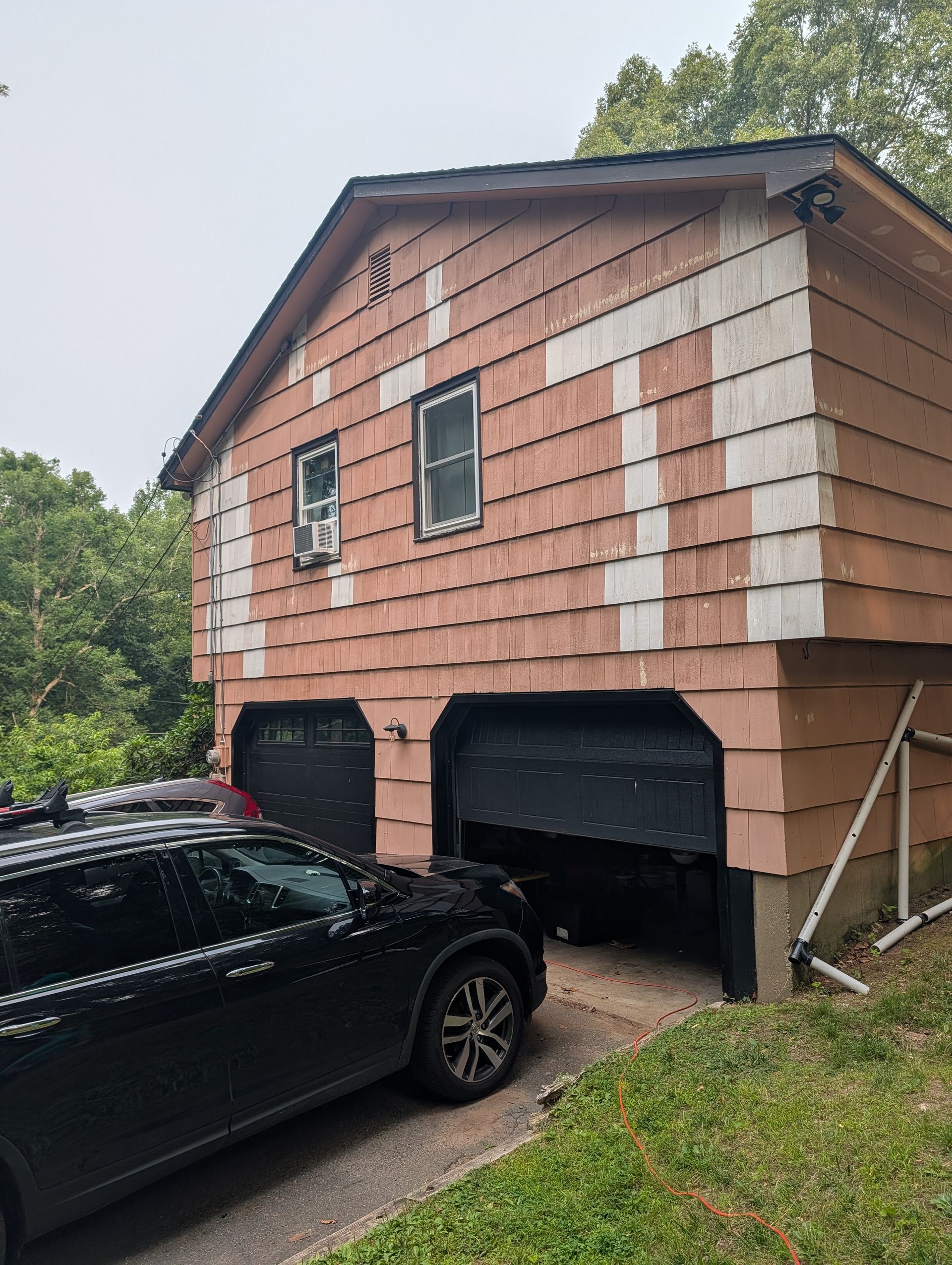 Two-story garage with red shingles and black doors, with a black SUV parked in front.