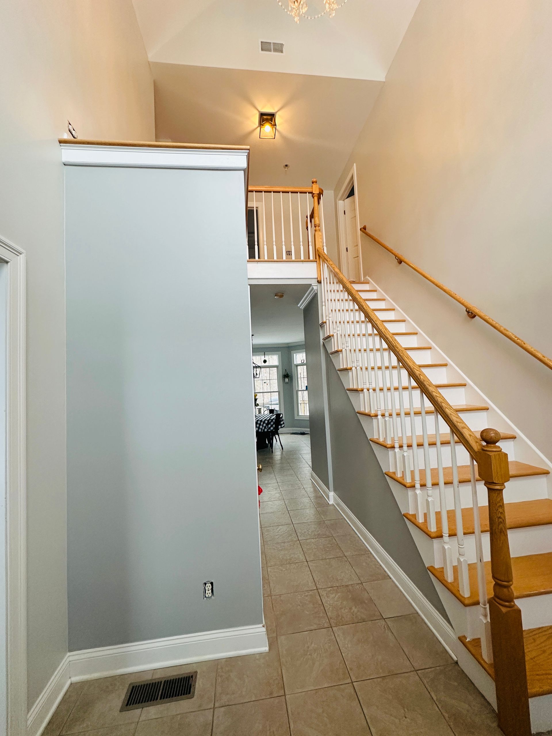 Narrow hallway with beige tile floor, gray walls, staircase on the right, and a ceiling light.