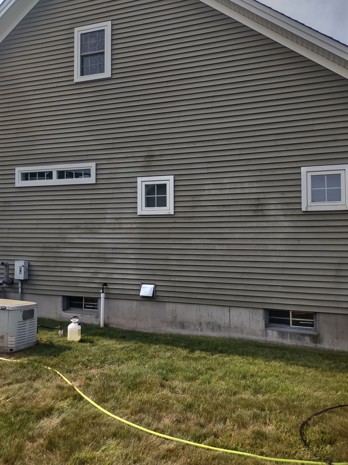 Side of a gray house with several windows, a lawn, and a yellow hose in the foreground.