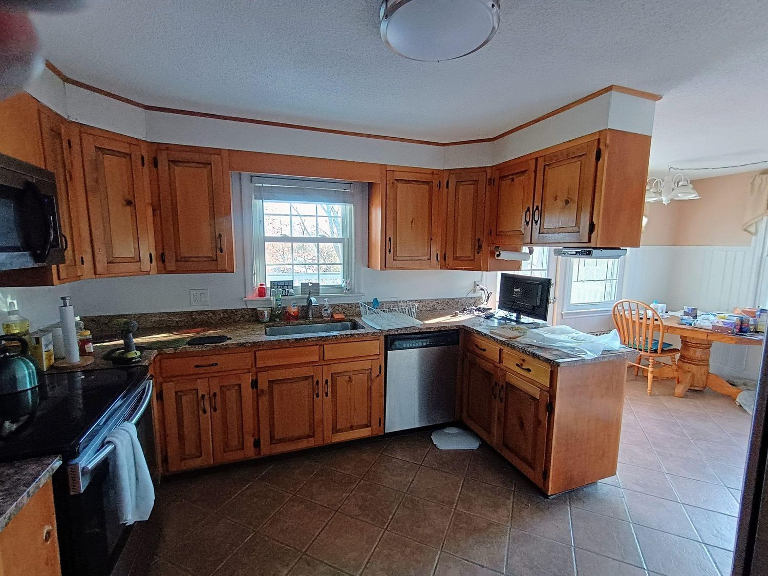 Wooden kitchen with granite countertops, stainless dishwasher, and a small dining area by the window.