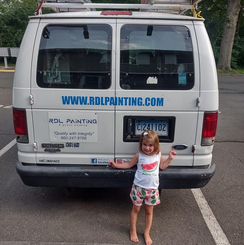 Little girl standing behind a white van with company decals and website text in a parking lot
