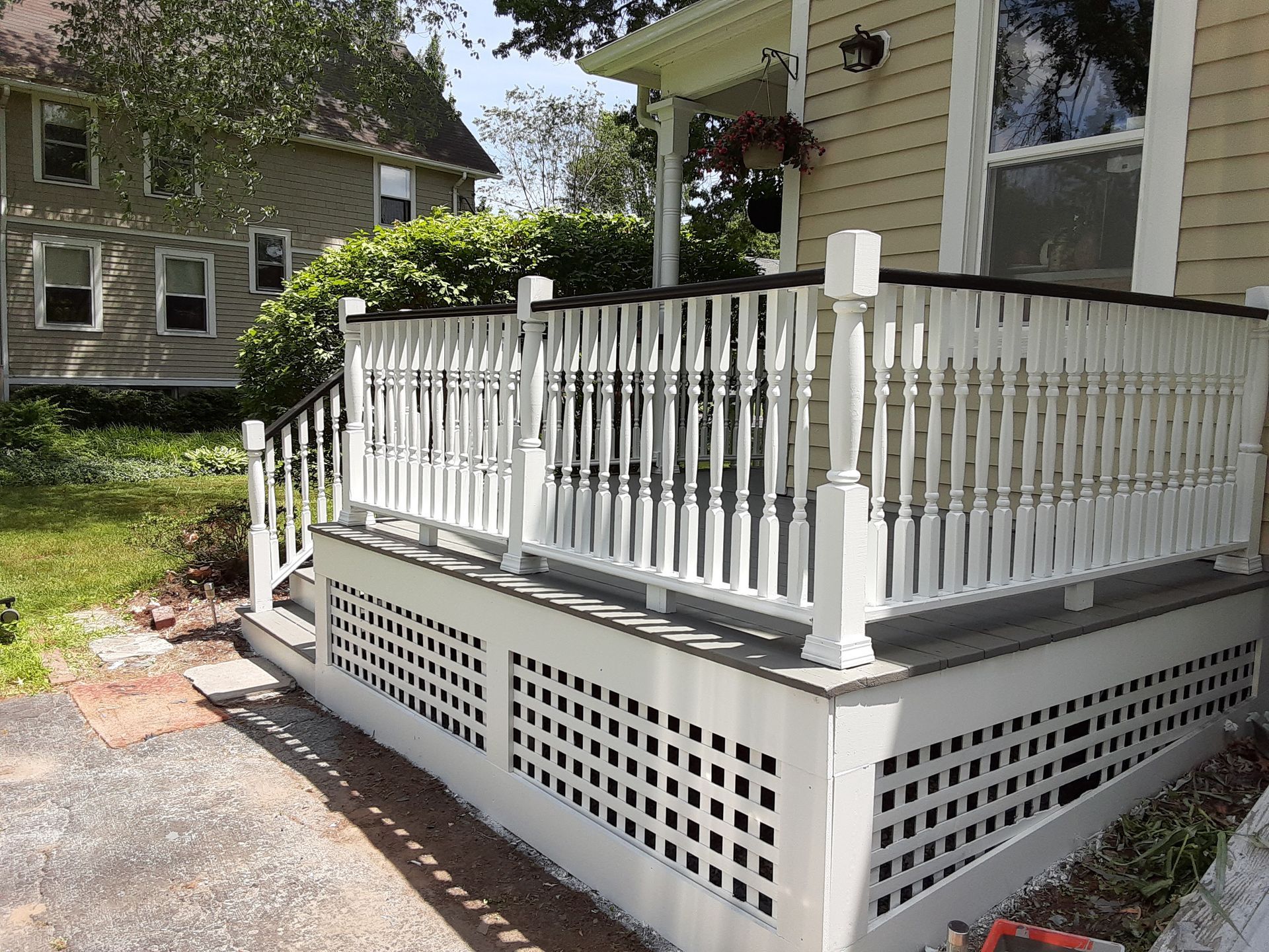 White house porch with white railing and lattice skirting beside a driveway and yard