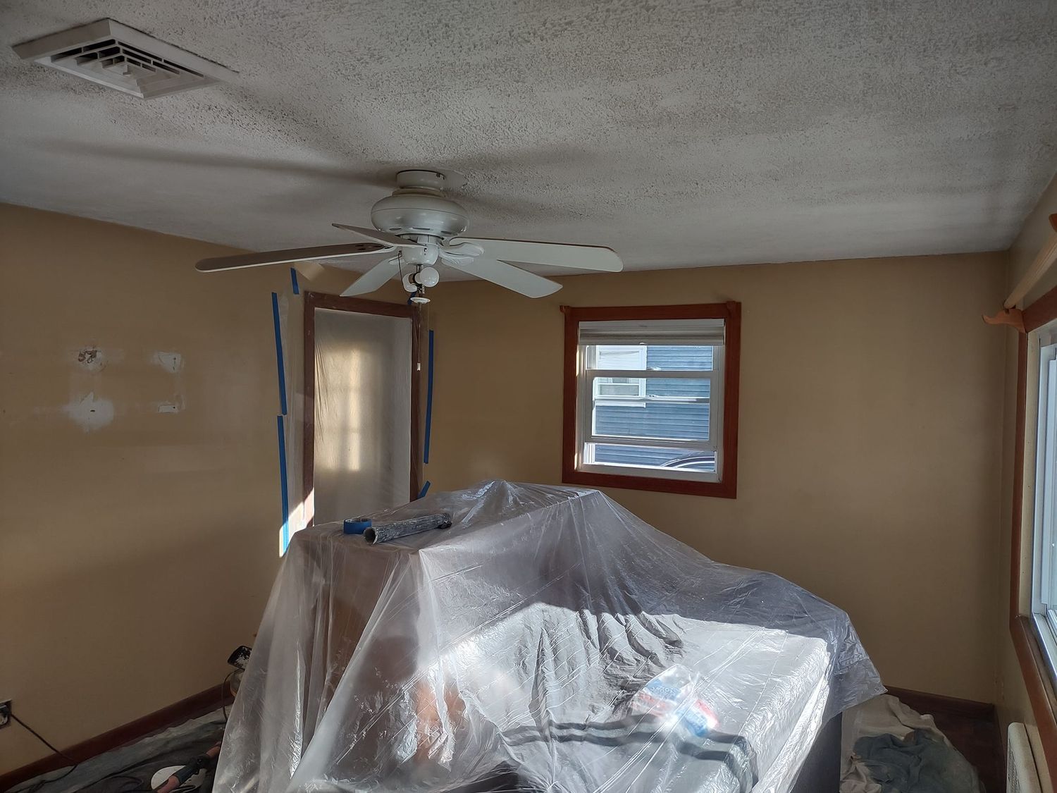 Living room with a plastic-covered couch, ceiling fan, beige walls, and a window with blinds.