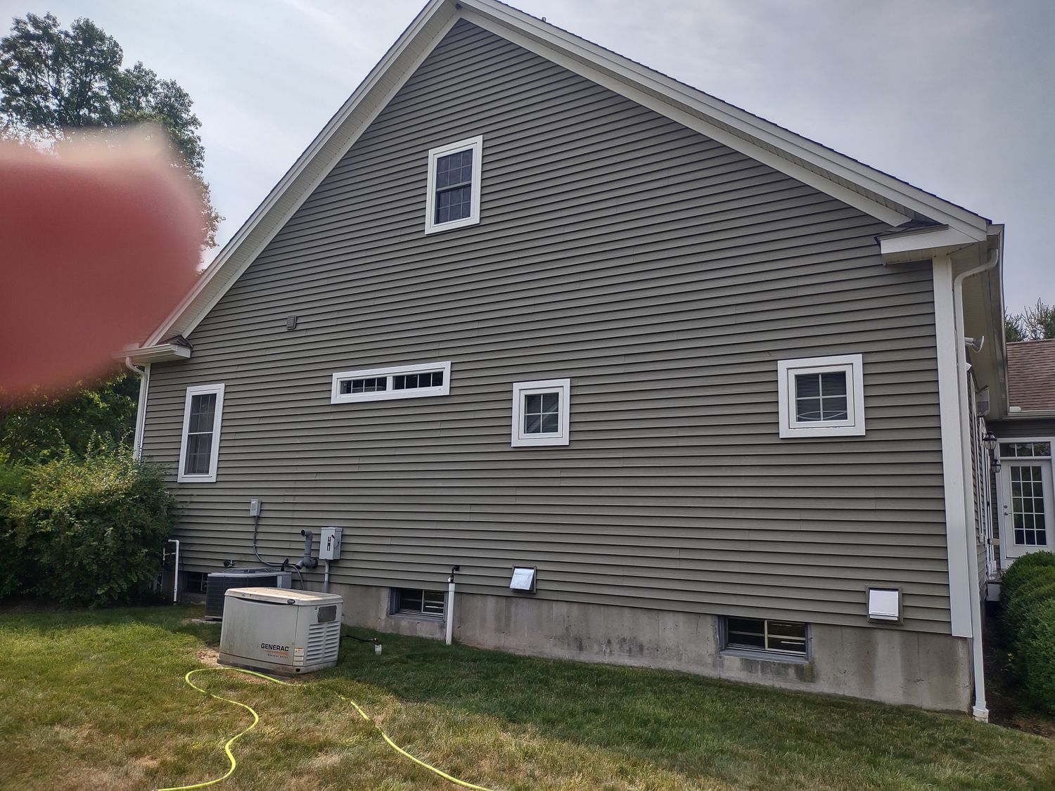 Side view of a gray house with white-trim windows and a person’s finger partly covering the lens.