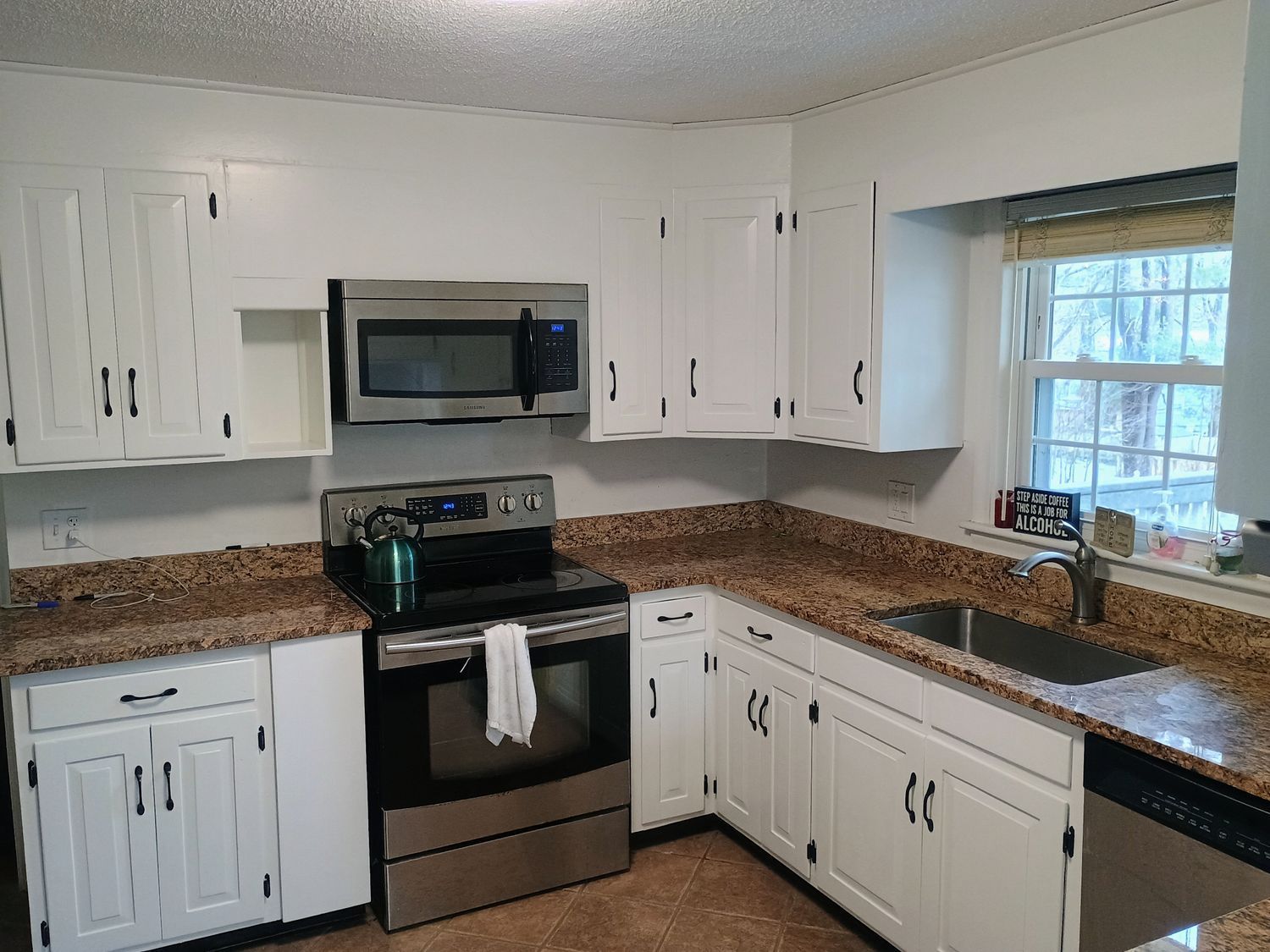Bright white kitchen with black appliances, granite counters, and a window over the sink