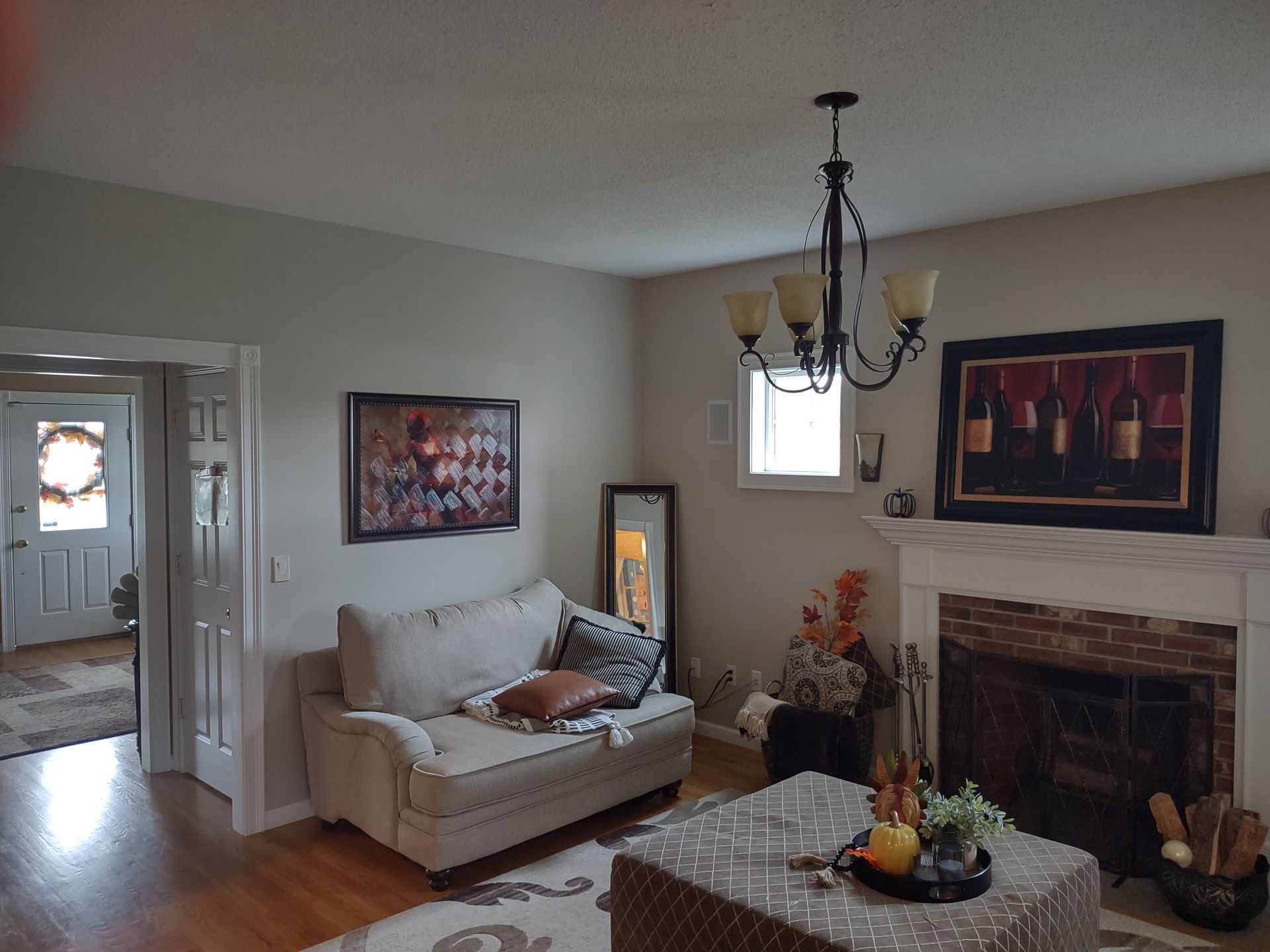 Bright living room with white sofa, chandelier, fireplace, coffee table, and an open doorway to another room