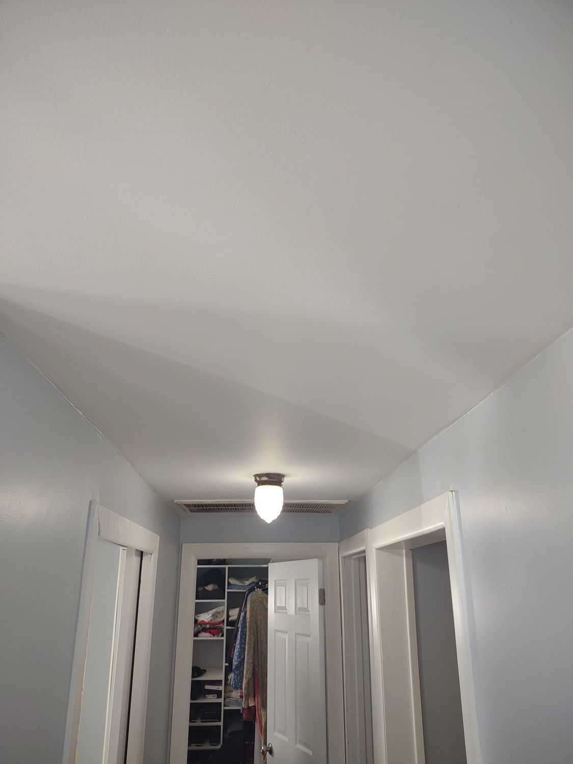 Narrow hallway with white walls, sloped ceiling, and a light fixture at the far end.