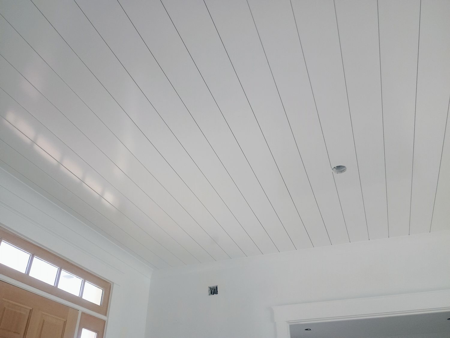 White room ceiling with narrow slats and a small wall opening near a windowed corner