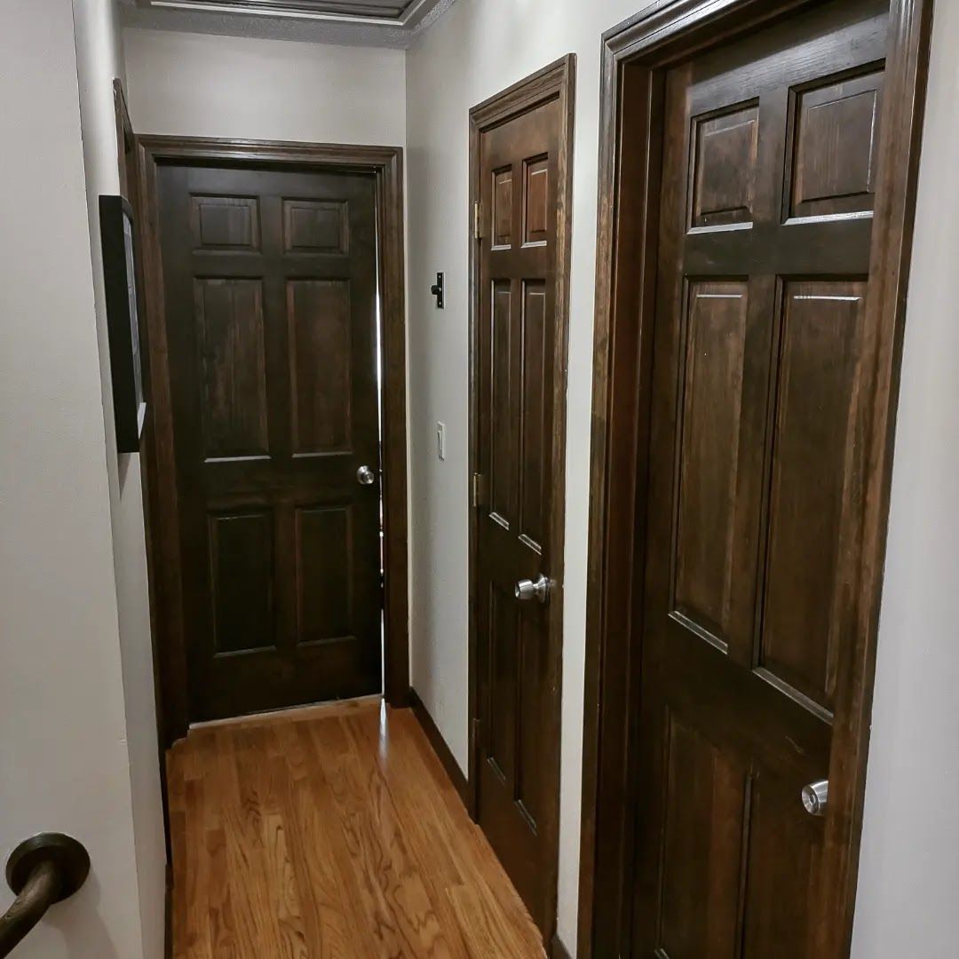 Narrow hallway with three dark wooden doors and hardwood floors.