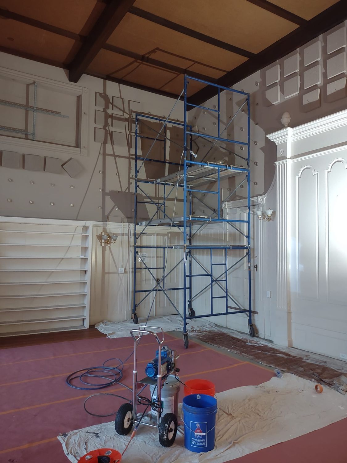 Blue scaffolding and painting supplies in a room with high ceiling and white walls