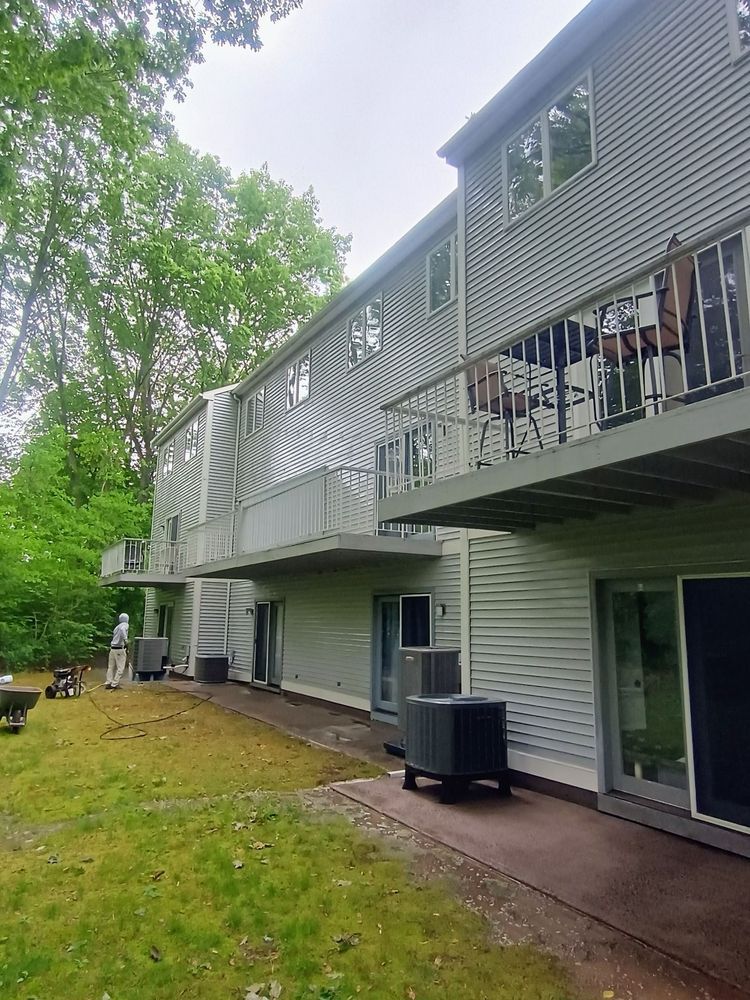 Backyard view of a raised house with white siding, deck railing, air conditioner, and grassy yard.