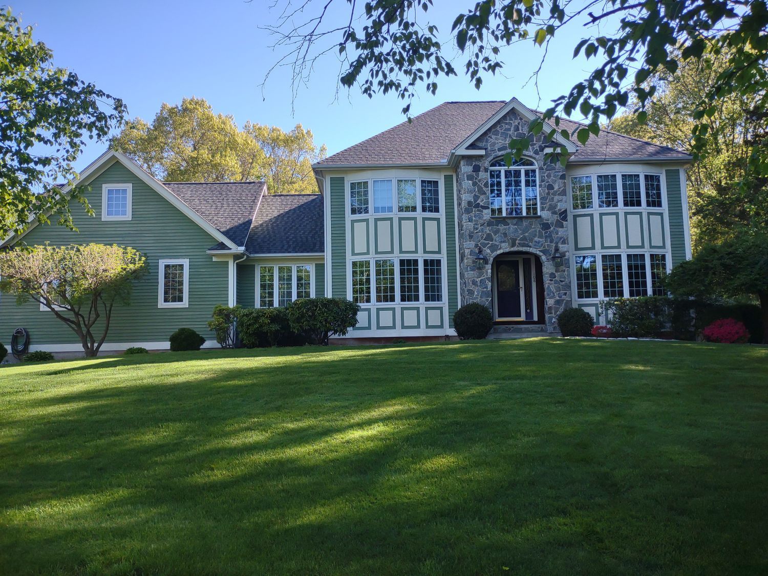 Large green house with Tudor-style facade, black-trimmed windows, and a wide front lawn under trees.