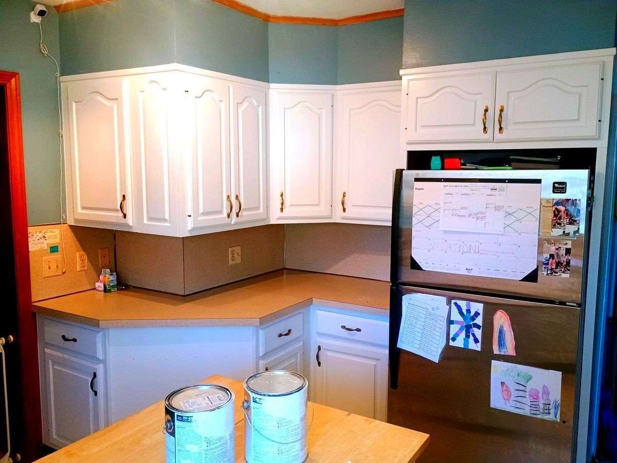 Kitchen with white cabinets, tan countertops, and a refrigerator covered with notes and drawings.