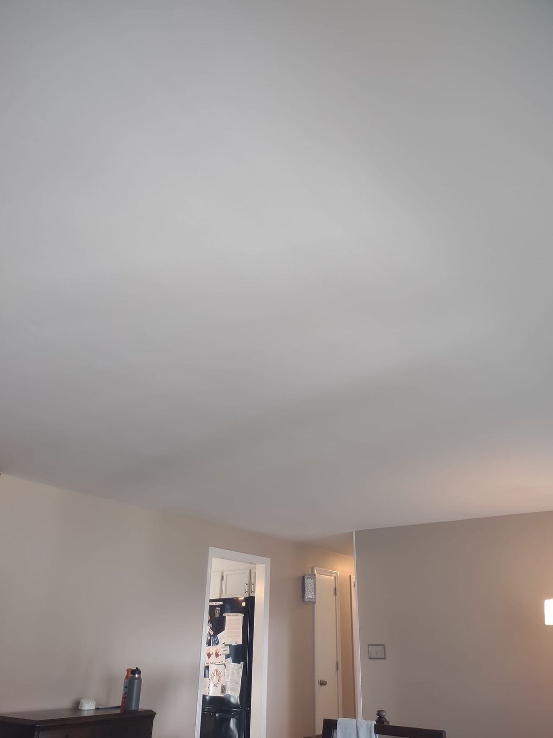 Interior room with beige walls, white ceiling, open doorway, and a dark dresser at left.