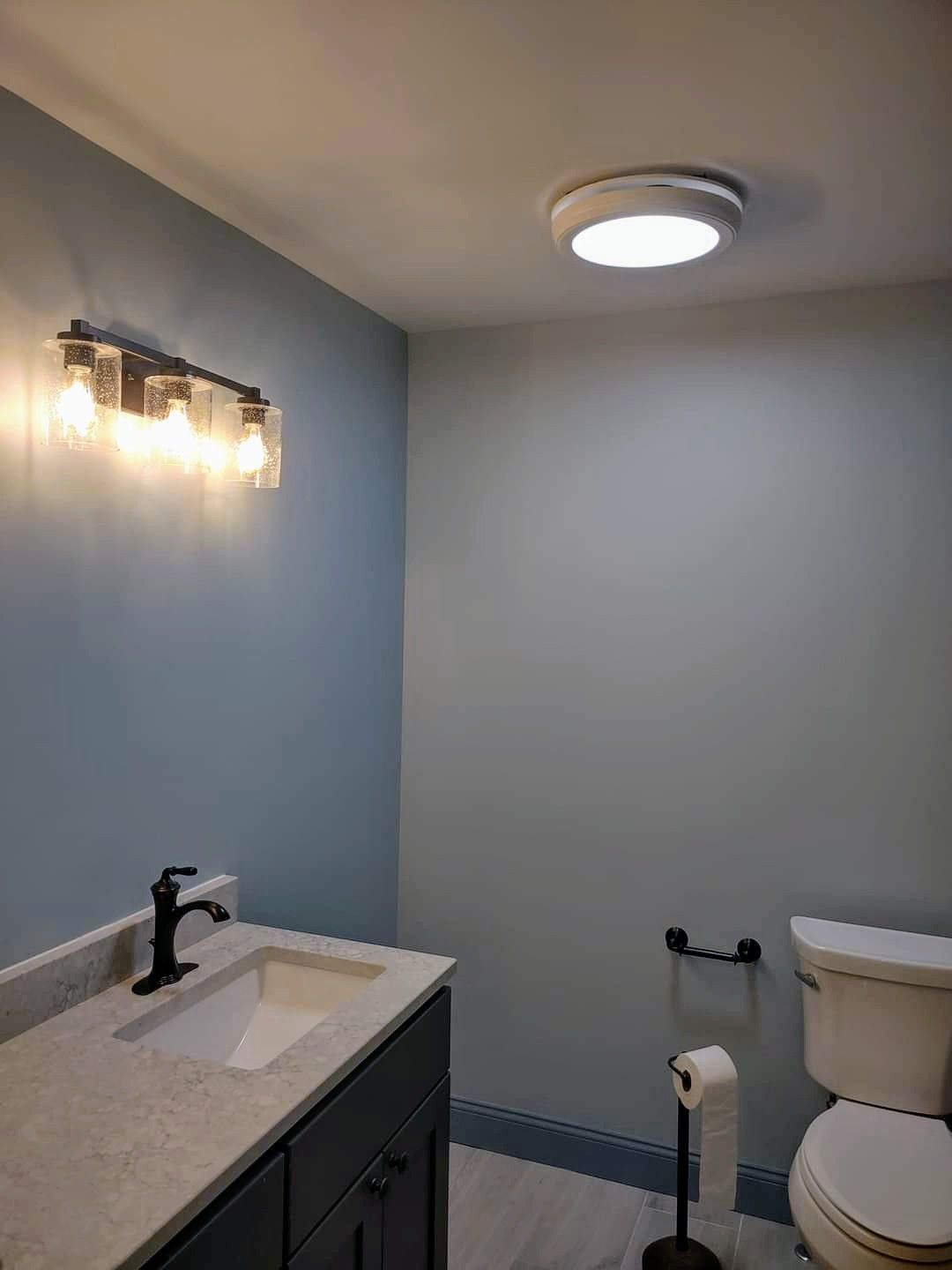 Small bathroom with blue and white walls, sink vanity, toilet, and wall light fixture.