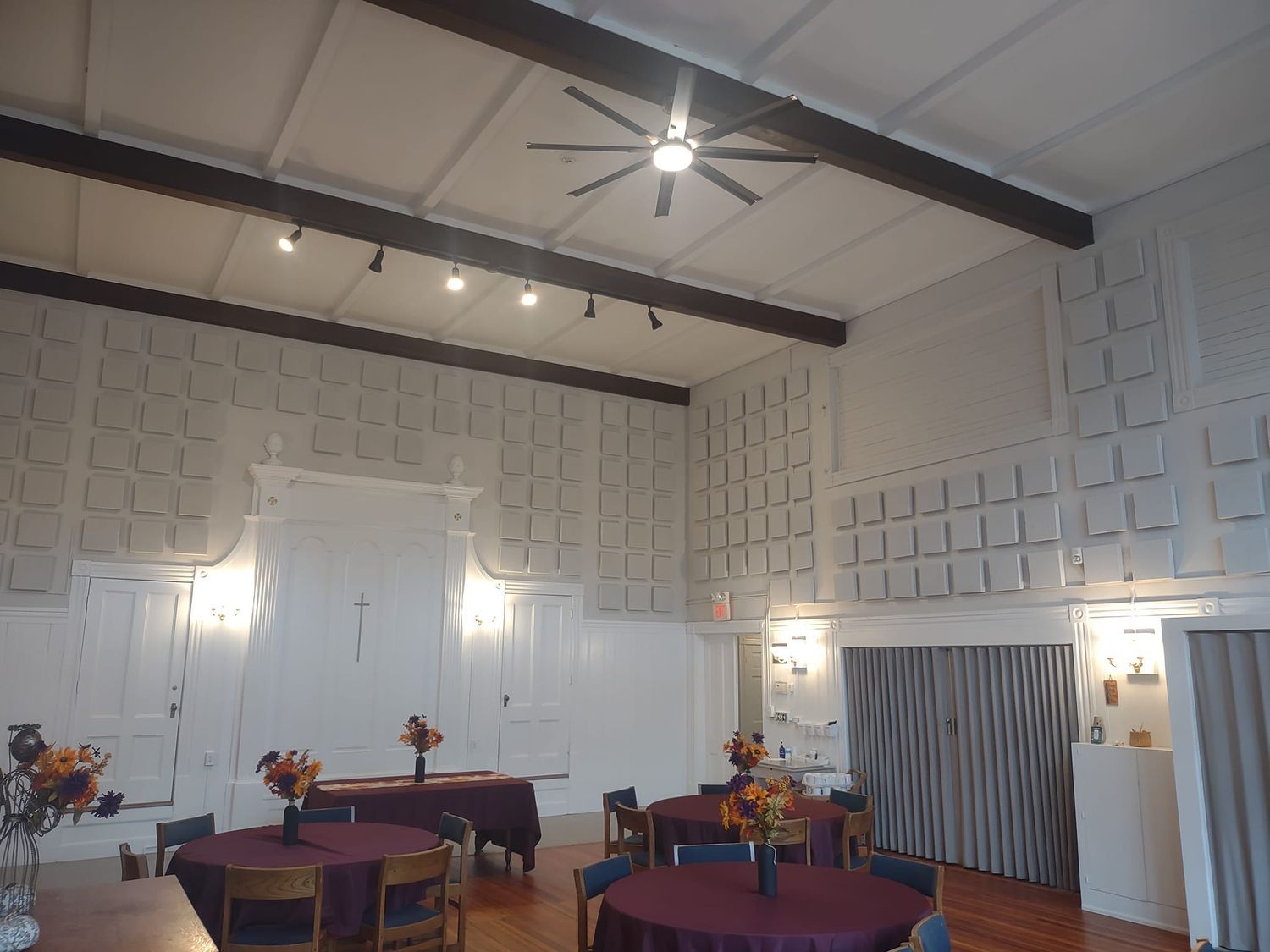 Elegant banquet hall with white paneled walls, dark ceiling beams, round tables, and floral centerpieces