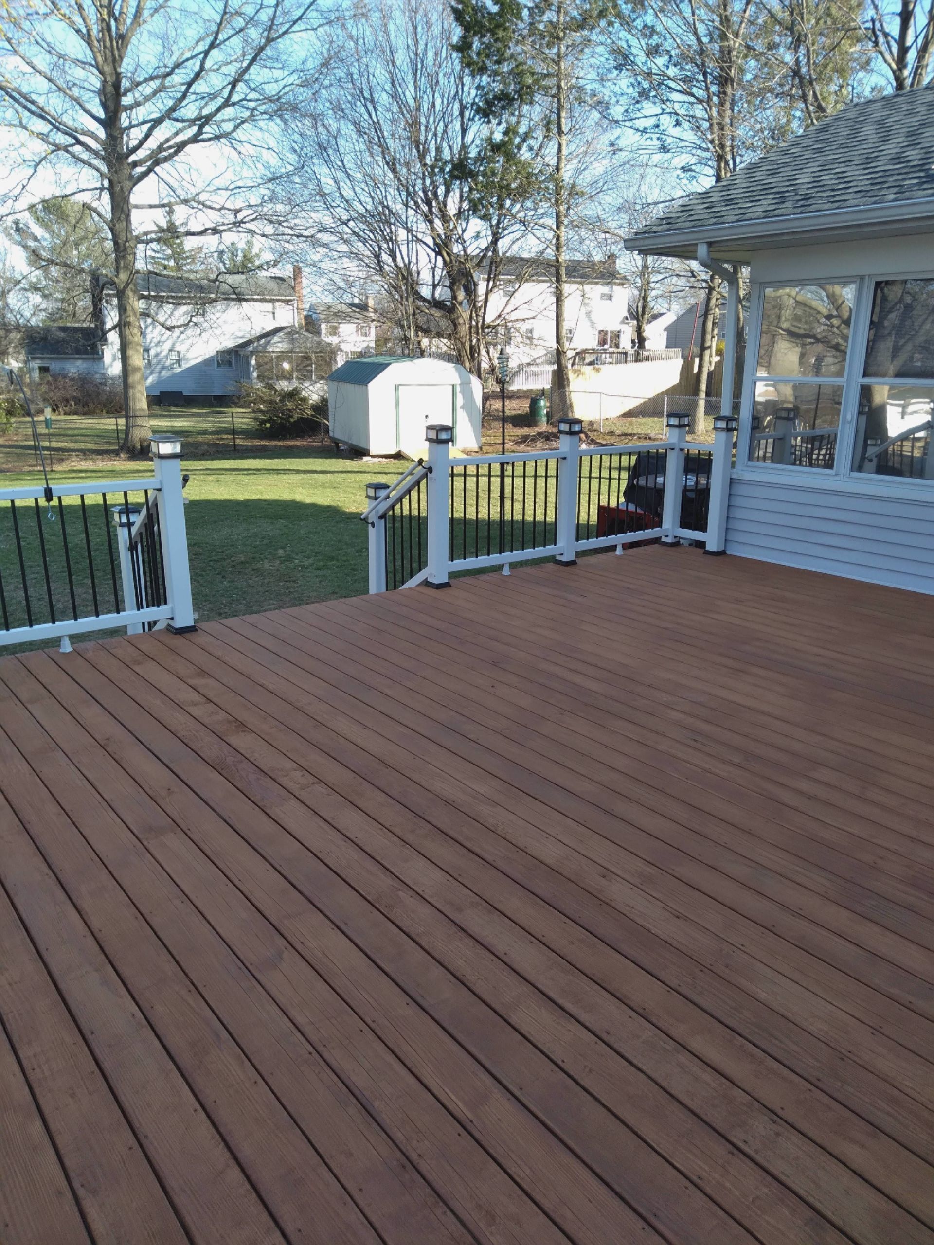 Wooden deck overlooking a fenced backyard with trees and a white shed.