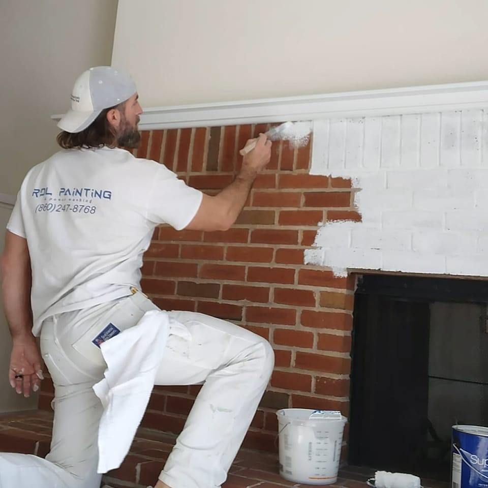 Painter applying white paint over brick fireplace wall indoors
