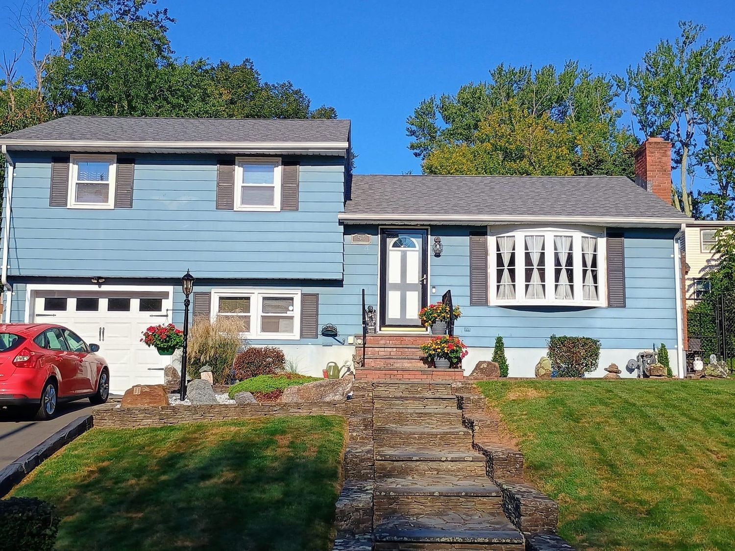 Blue two-story house with a front lawn, stone steps, and a red car in the driveway