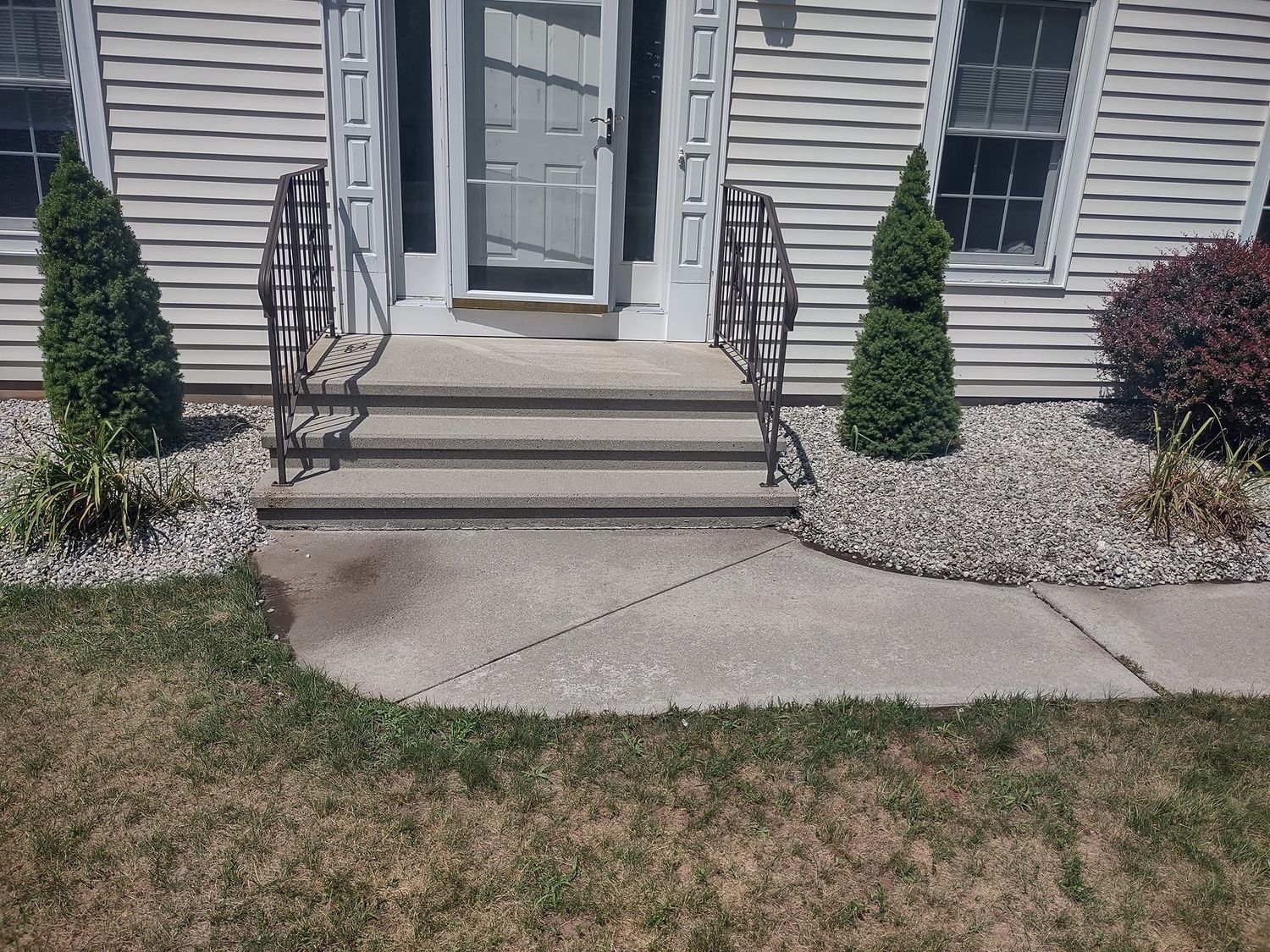 Front steps to a gray house with white door, black railings, and flower beds along the walkway.