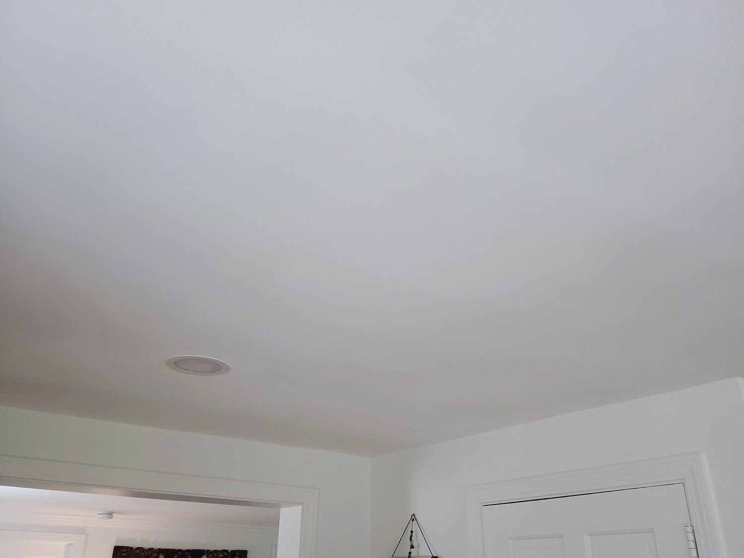 White ceiling and upper walls of a room with a smoke detector and window trim visible