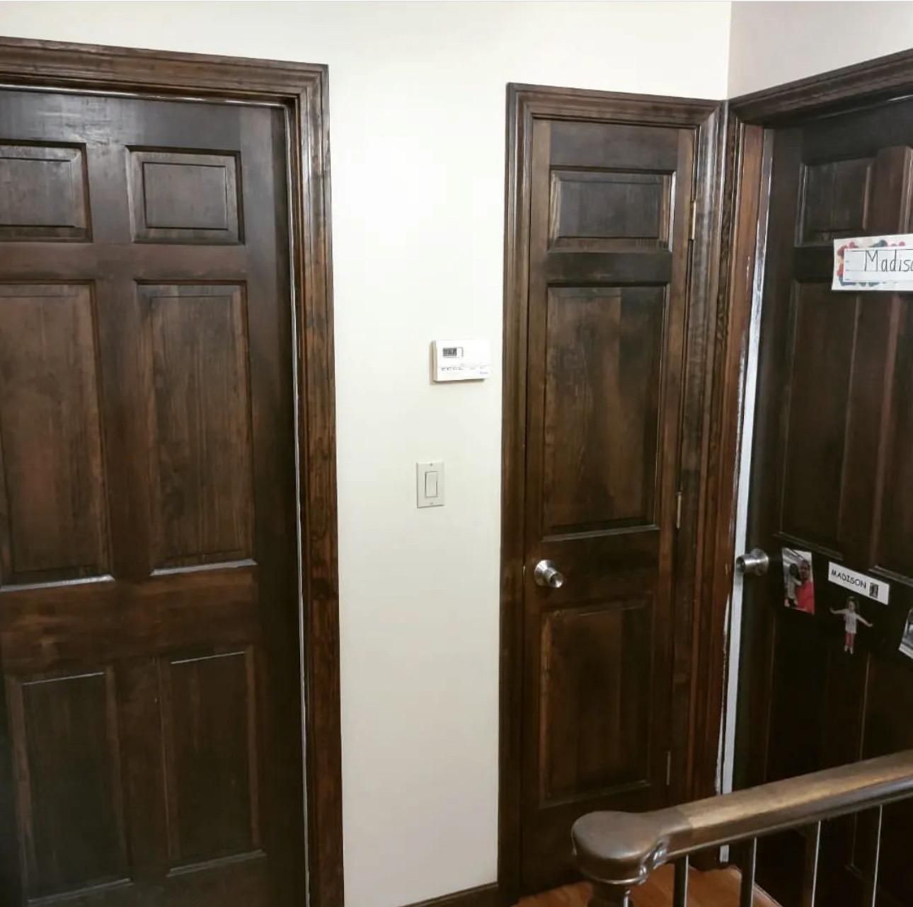 Wooden interior doors in a hallway, with a stair railing in the foreground.