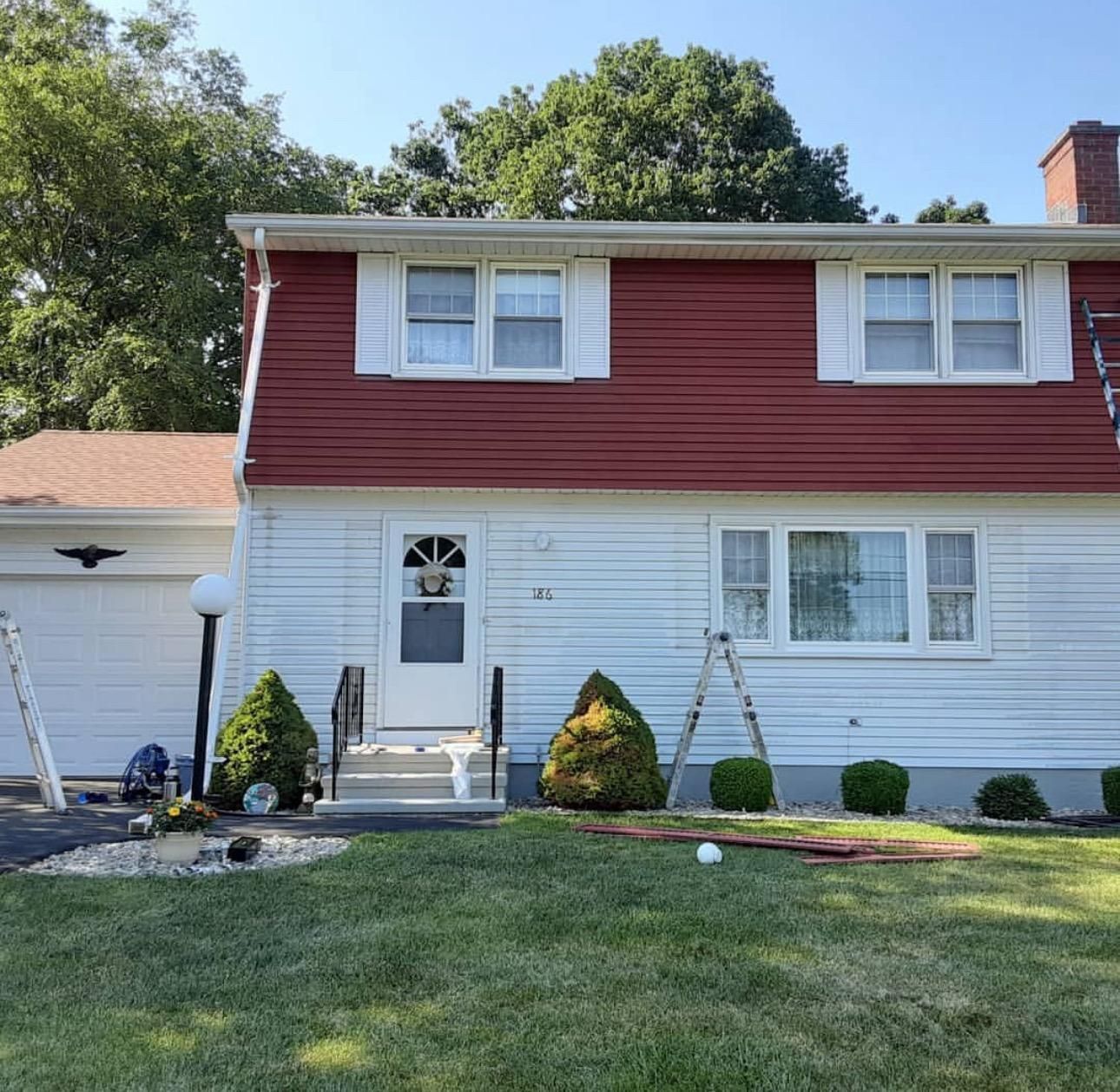 Two-story house with red upper siding and white lower siding, front door, garage, and landscaped yard