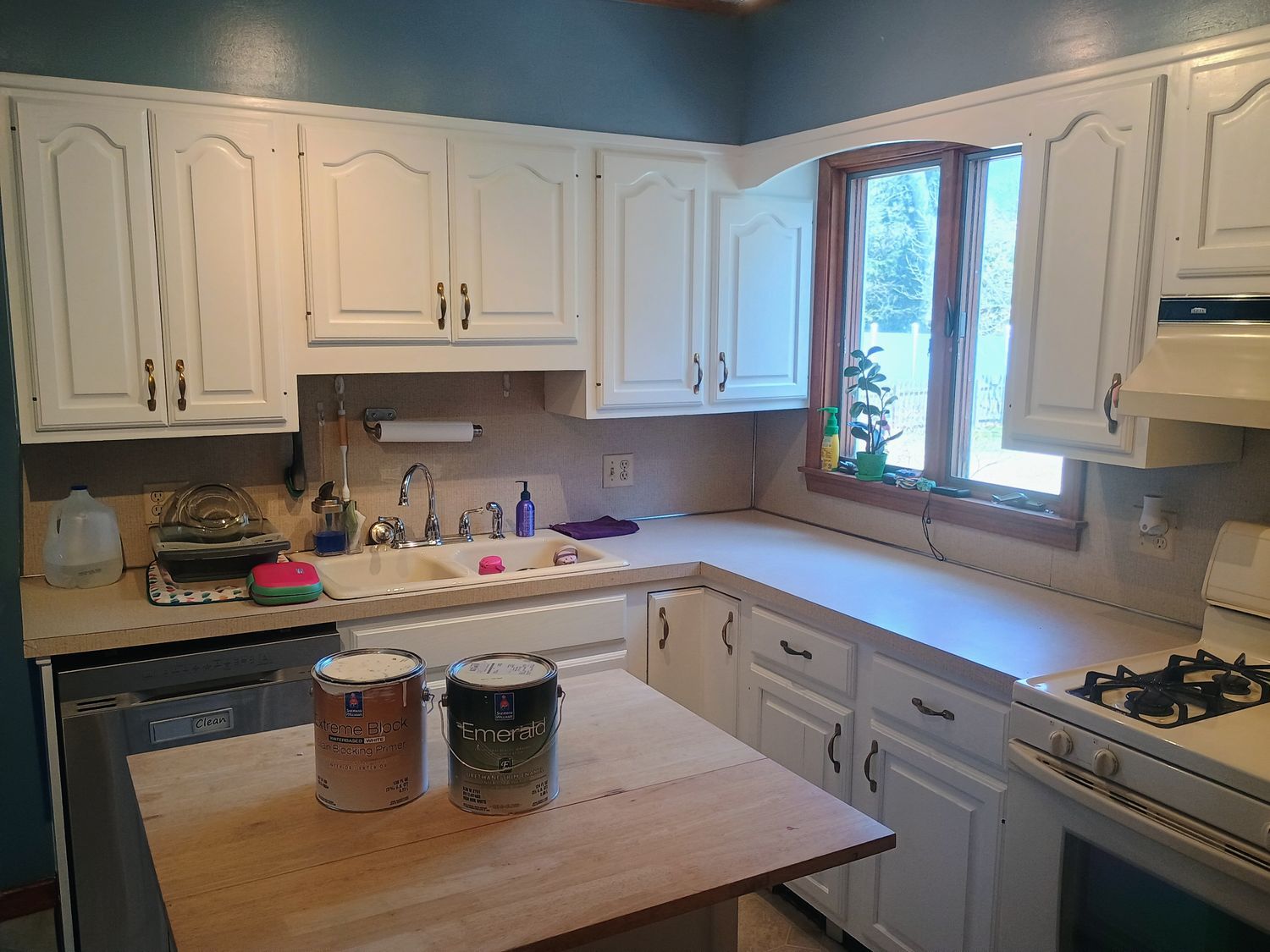 Bright kitchen with white cabinets, wood island, sink under window, and a gas stove.