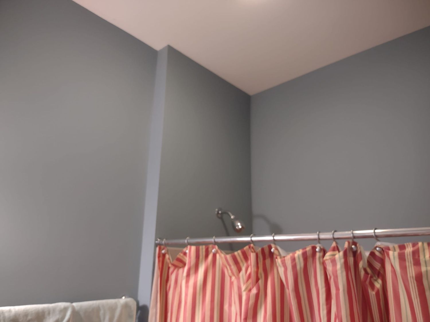 Gray room corner with a shower curtain rod and pink striped curtain partially visible below