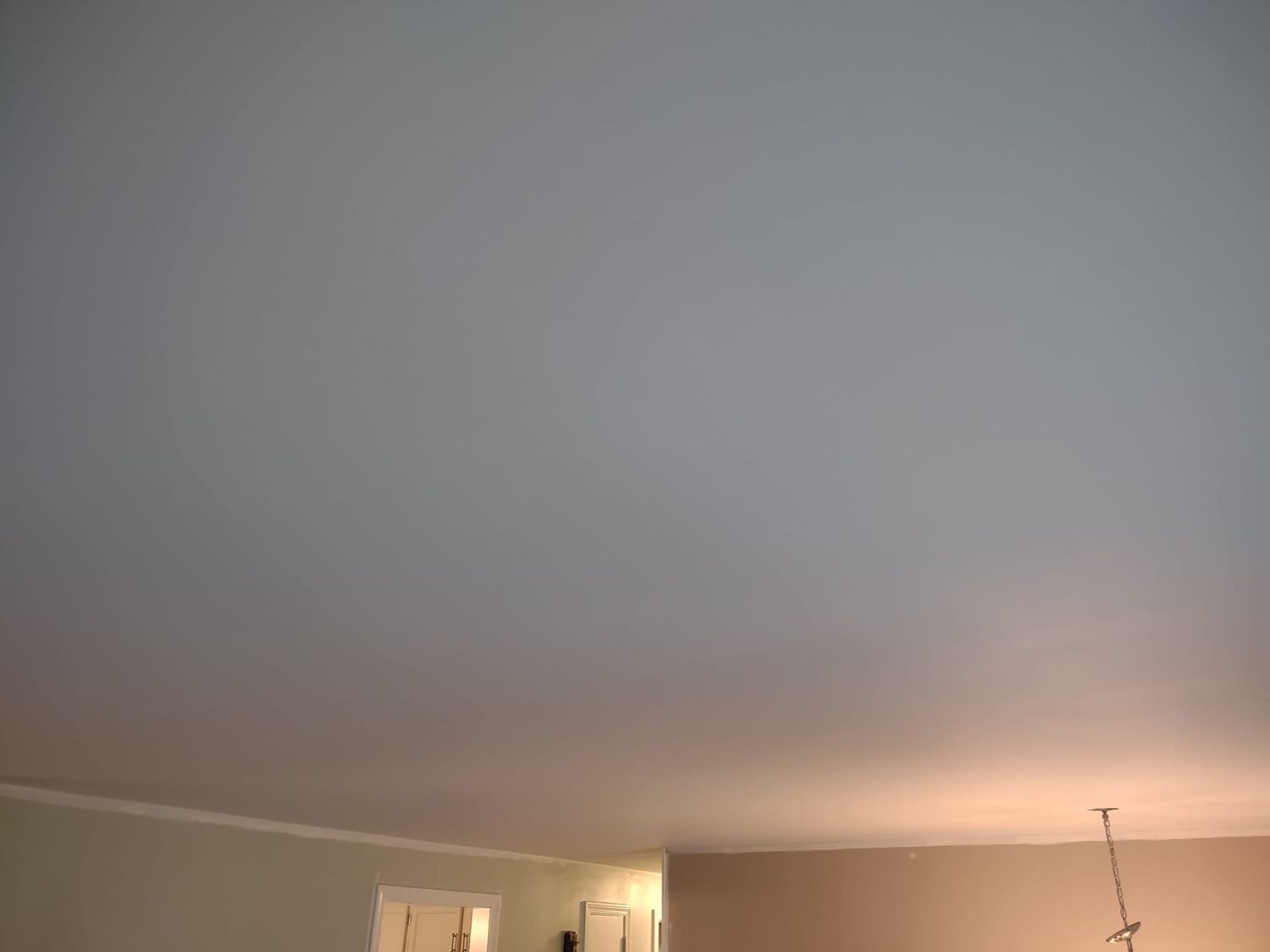 Blank ceiling above a room corner, with warm light from a doorway below