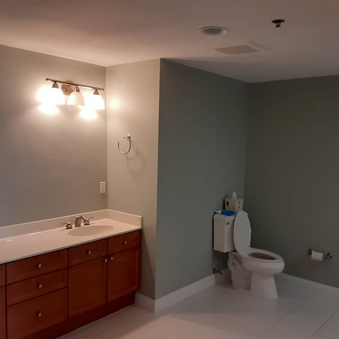Small bathroom with gray walls, white toilet, and wooden vanity with mirror lights.