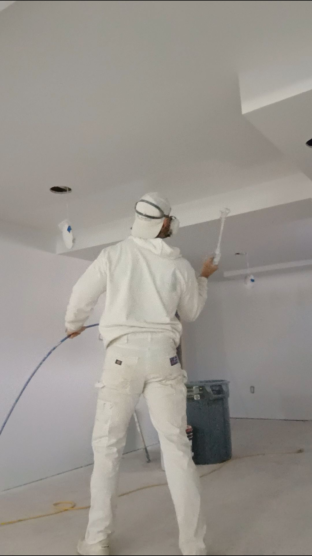 Person in white workwear painting a white ceiling in an unfinished room.