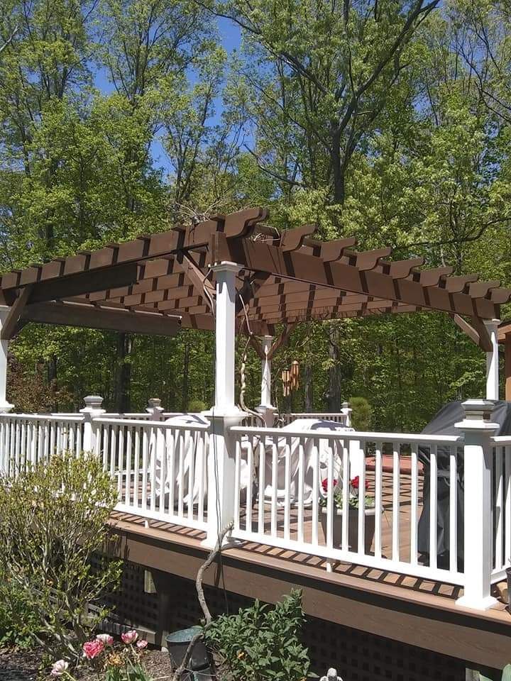 White-railed wooden deck with pergola in a leafy backyard garden, with flowers below