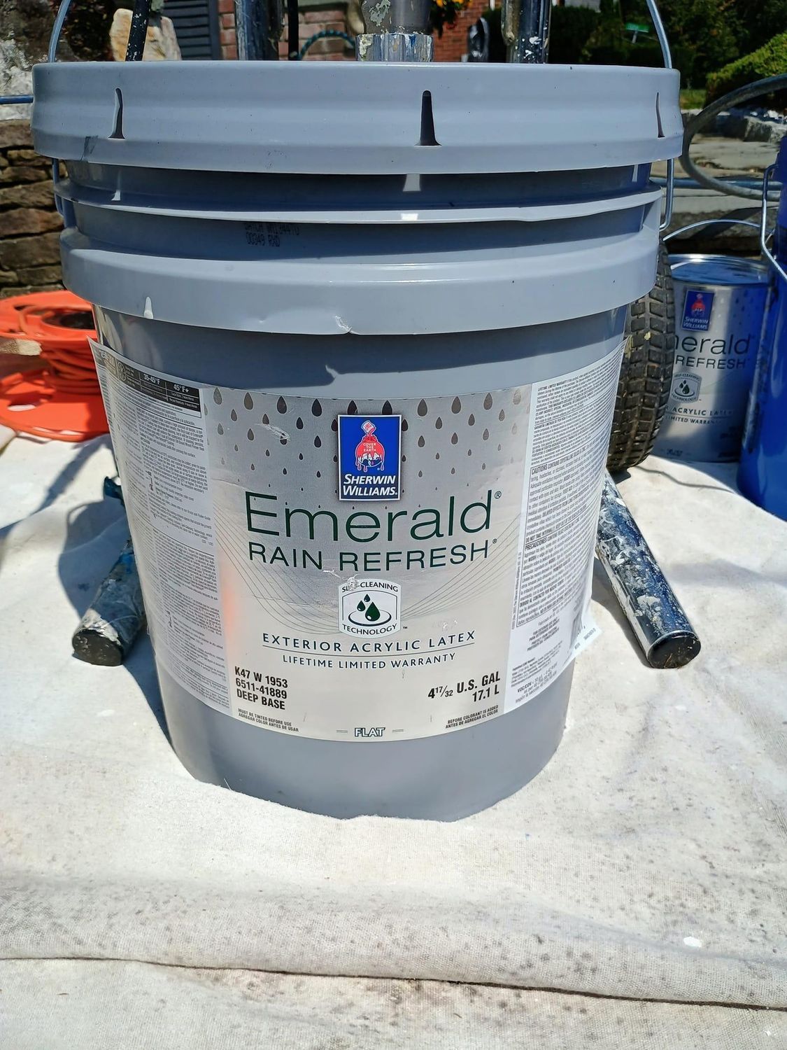 Gray bucket of Emerald rain refresh paint on a white surface outdoors