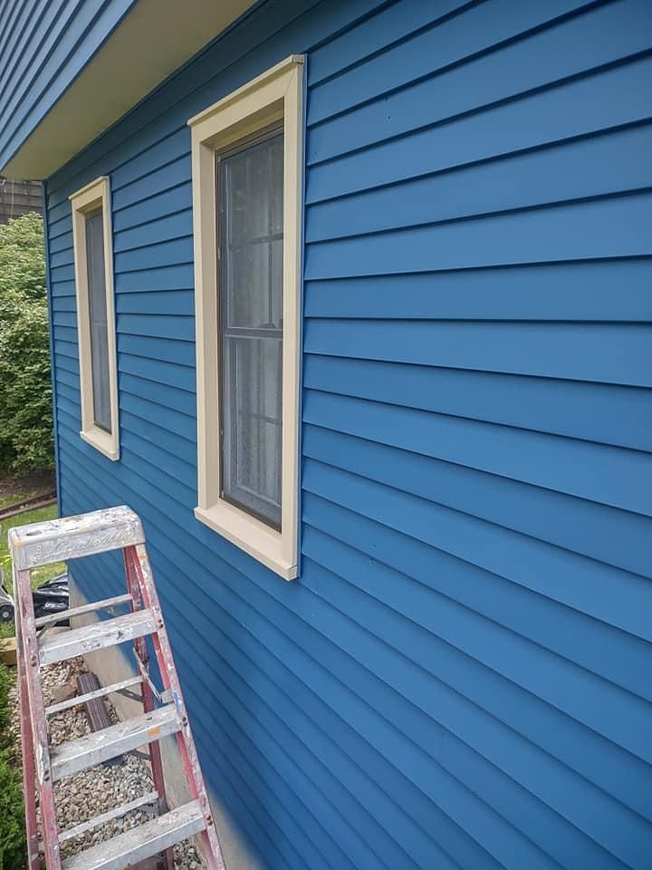 Blue house exterior with beige-trimmed windows and a ladder leaning against the siding