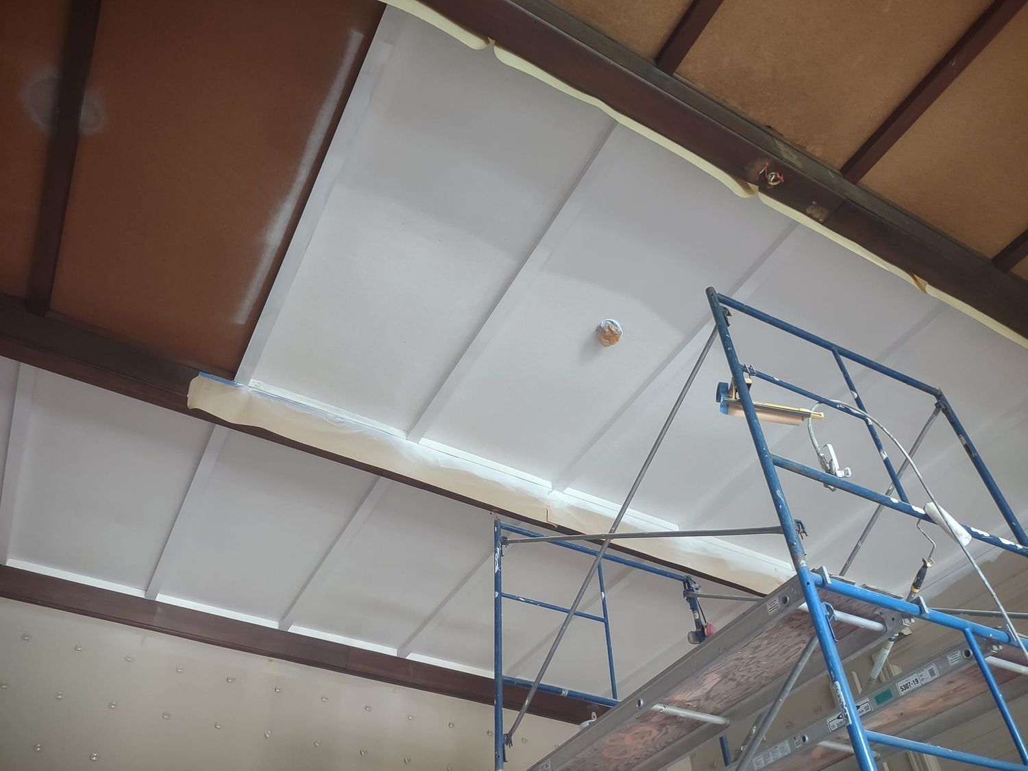 Blue scaffolding inside a building with a white ceiling and wooden roof panels