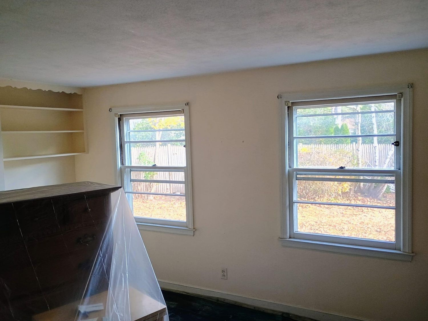 Small empty room with beige walls, two windows, and shelves near a covered counter.