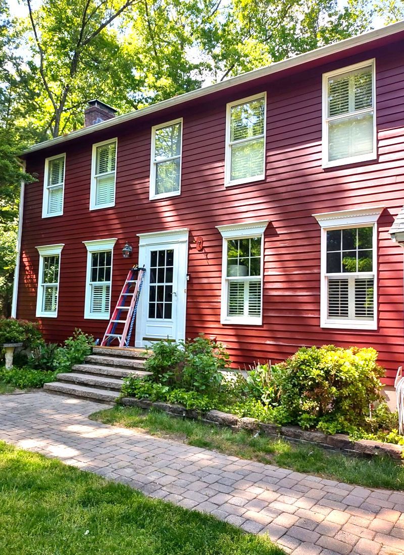 Red two-story house with white-trim windows and a centered front door, beside a brick walkway and greenery