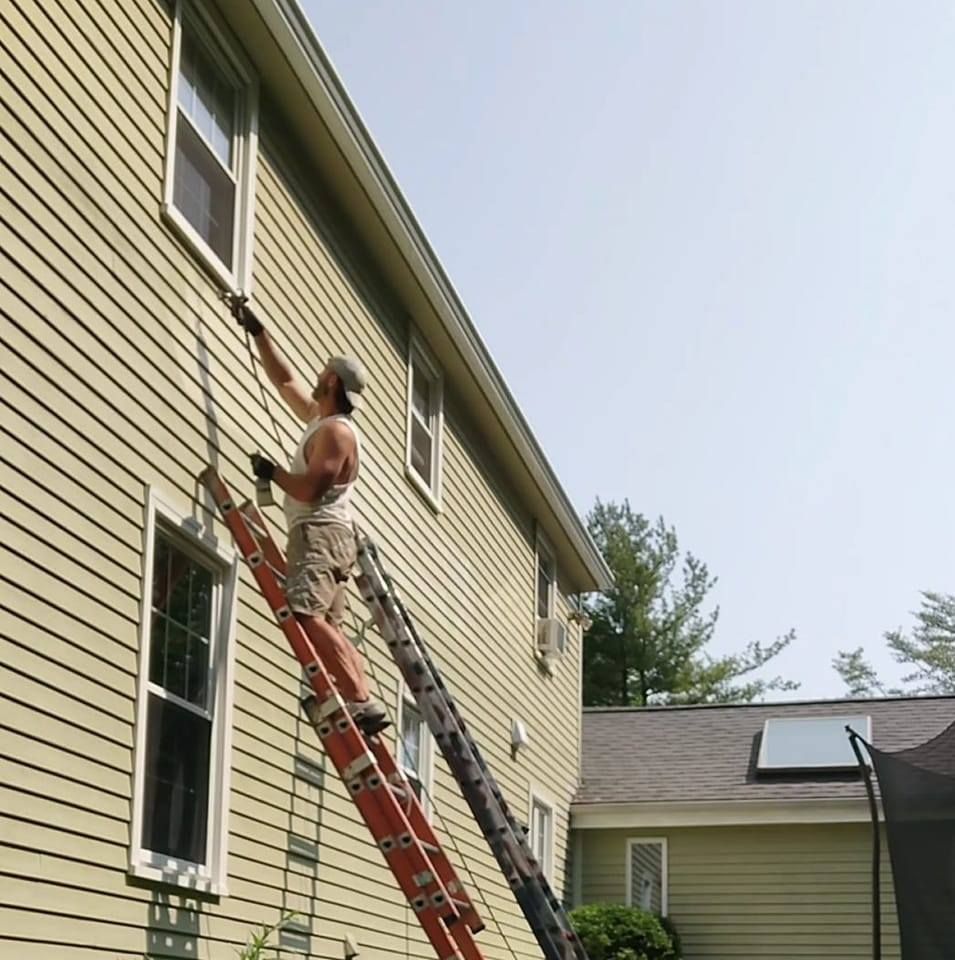 Worker on a ladder painting the upper siding of a house
