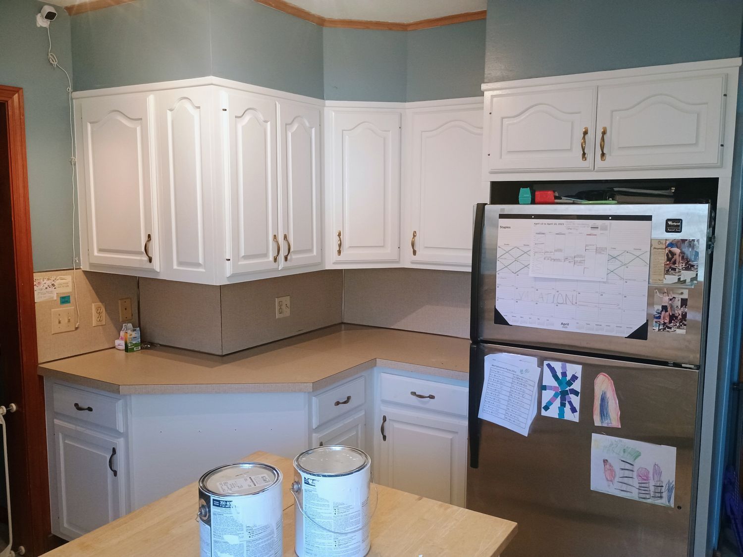 Small kitchen with white cabinets, beige countertops, and a refrigerator covered with notes and papers.