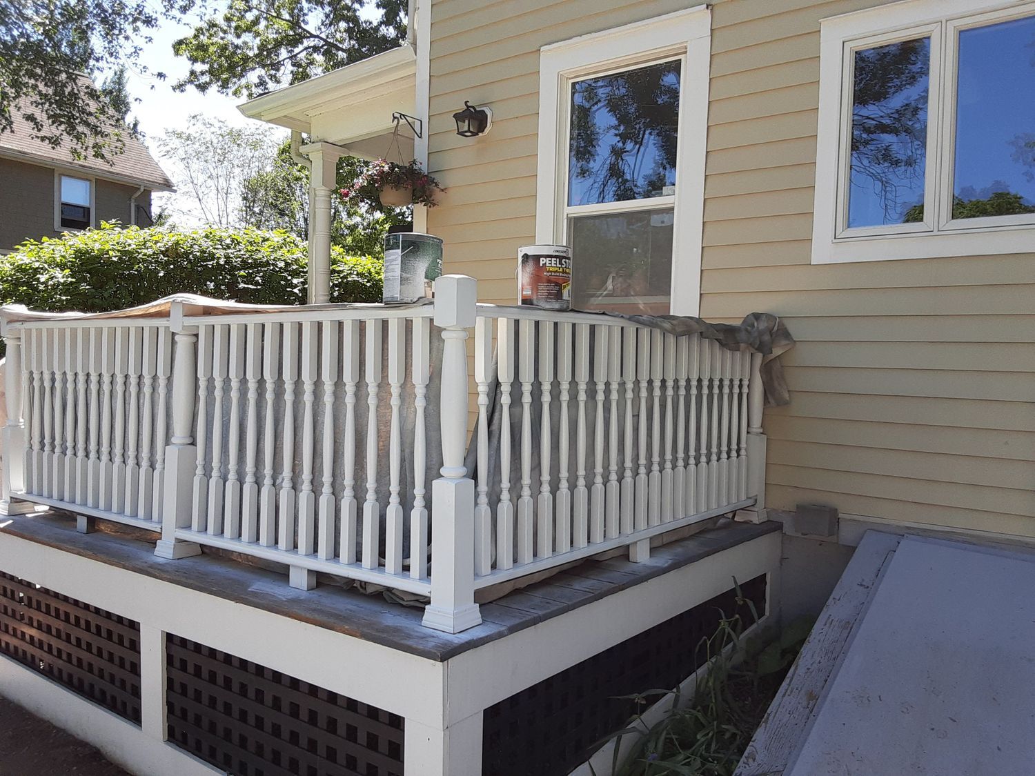 Small front porch with white railing on a beige house, beside a window and door.