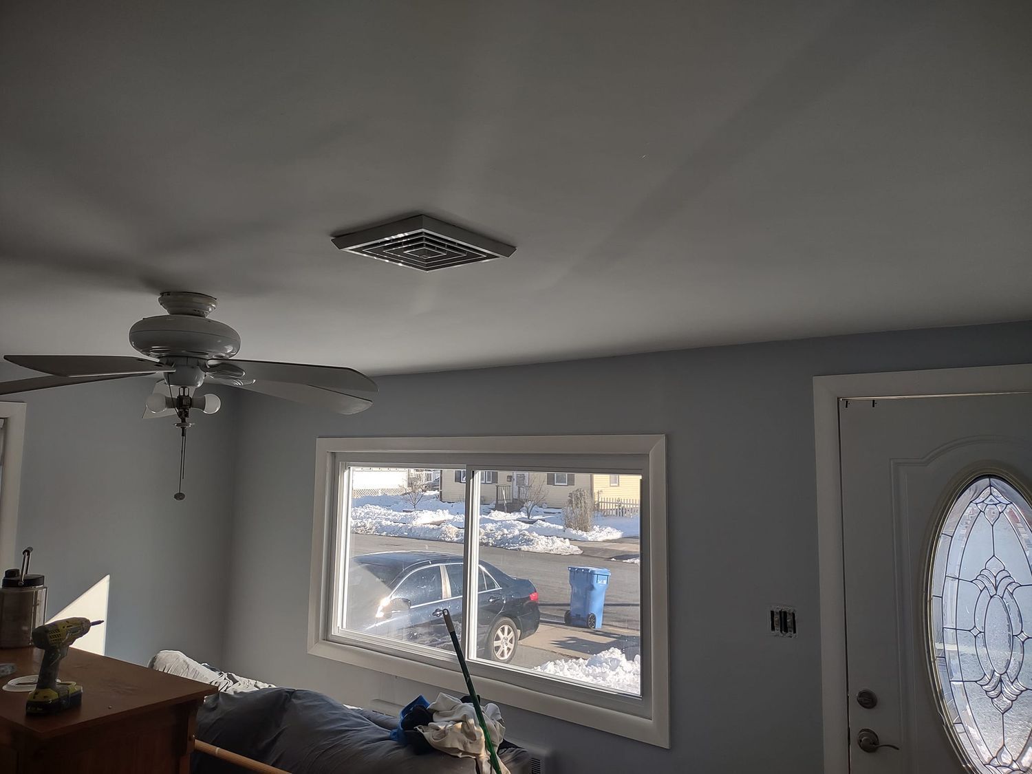 Living room with gray walls, ceiling fan, window, and front door with frosted oval glass.