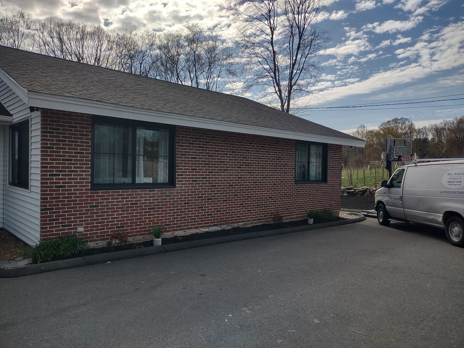 Brick house exterior with dark shutters, a white van parked beside it, and a cloudy sky.