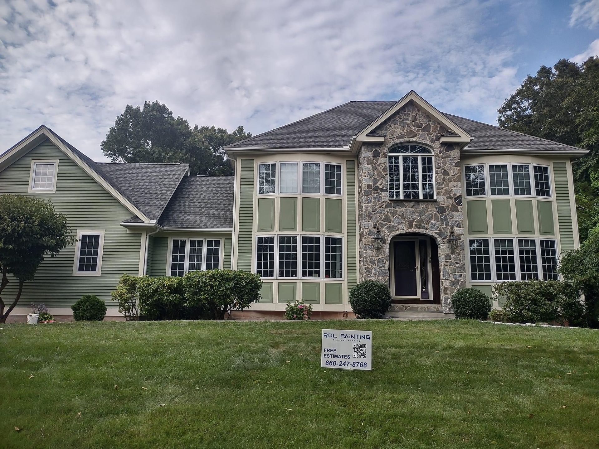 Large two-story cream house with green shutters, front lawn, and a sign in the yard