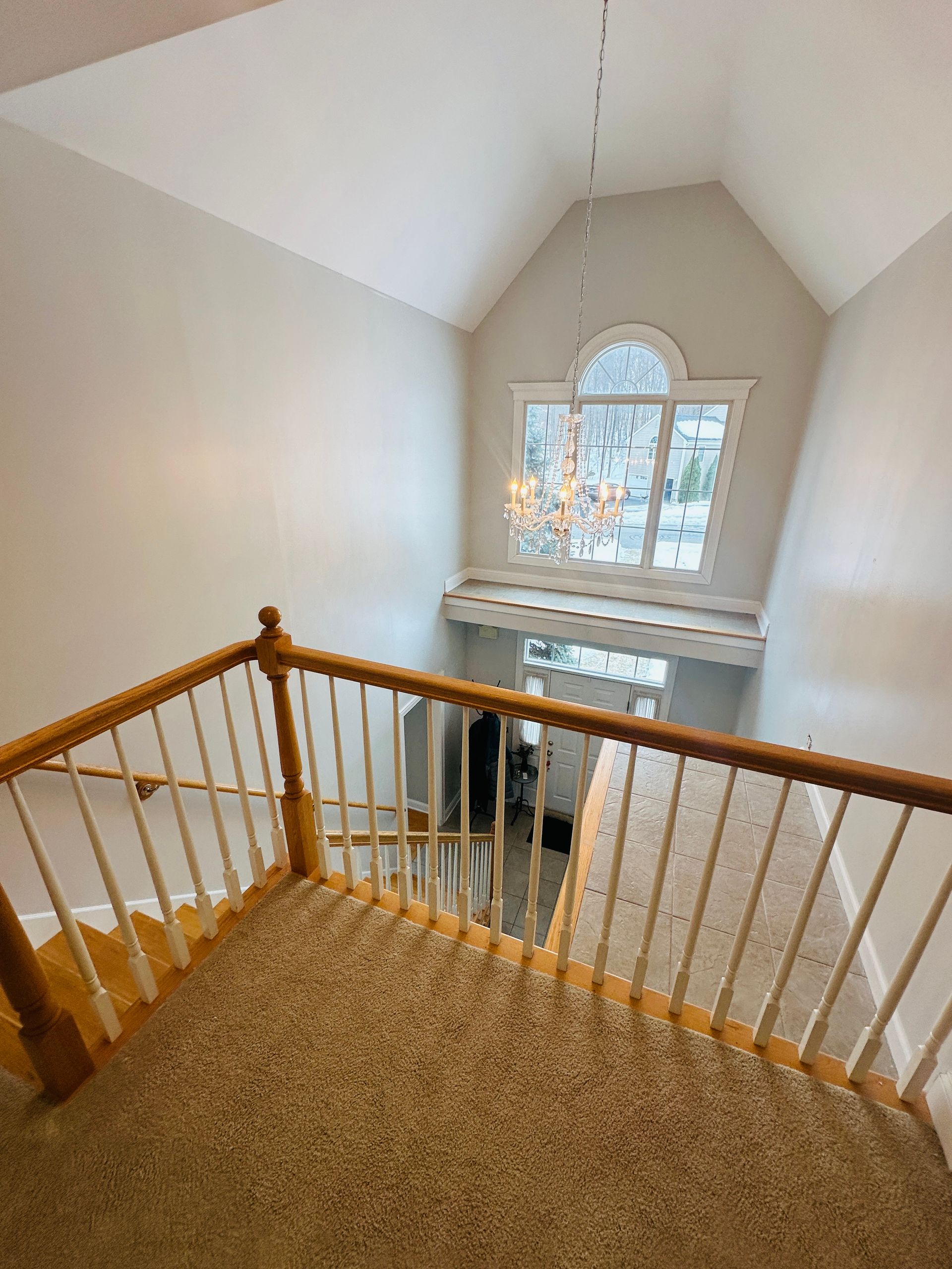 Interior landing with carpeted stairs, white walls, and a large arched window overlooking a lower floor